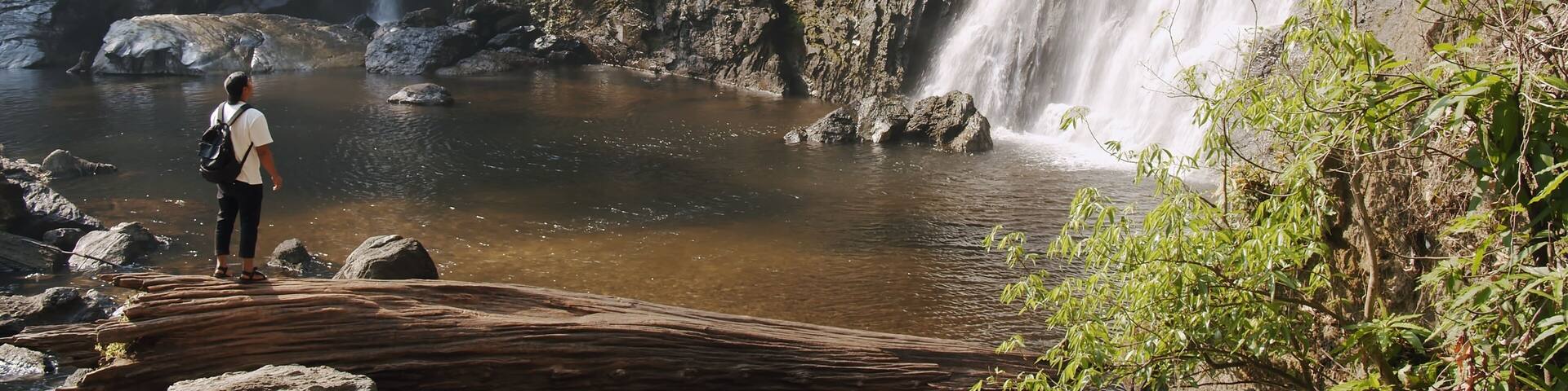 Young tourist traveler man standing enjoy wonderful tropical amazing Khlong Lan Waterfall in Klong Lan National Park, beautiful falling water at Kamphaeng Phet, Thailand, Travel vacation nature