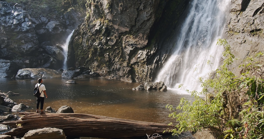 Young tourist traveler man standing enjoy wonderful tropical amazing Khlong Lan Waterfall in Klong Lan National Park, beautiful falling water at Kamphaeng Phet, Thailand, Travel vacation nature