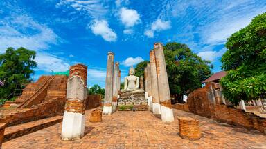 A large Buddha statue in a temple with brick ruins and a clear blue sky.