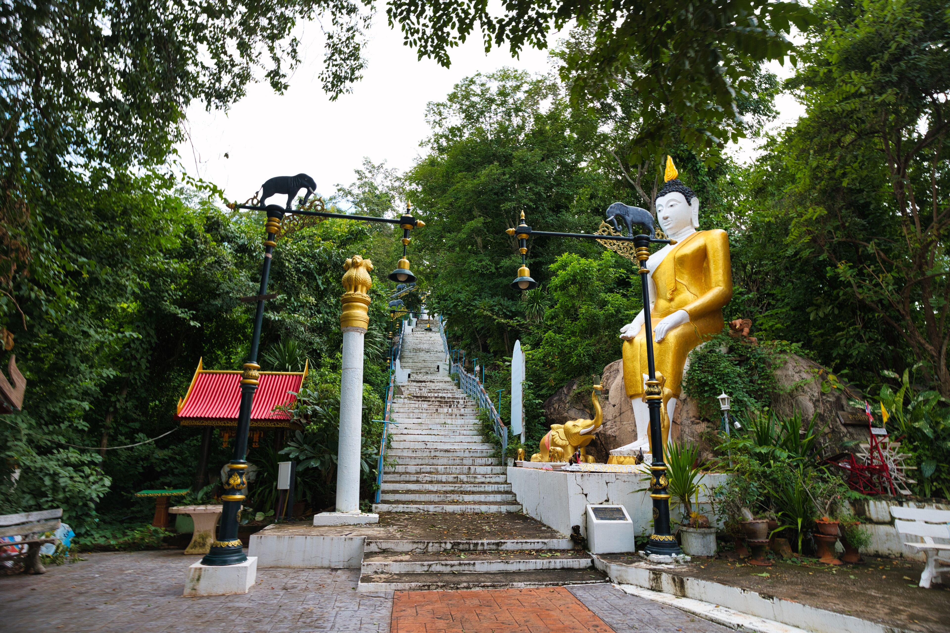 A temple with a golden statue, a white statue, and a black statue on a staircase surrounded by greenery.