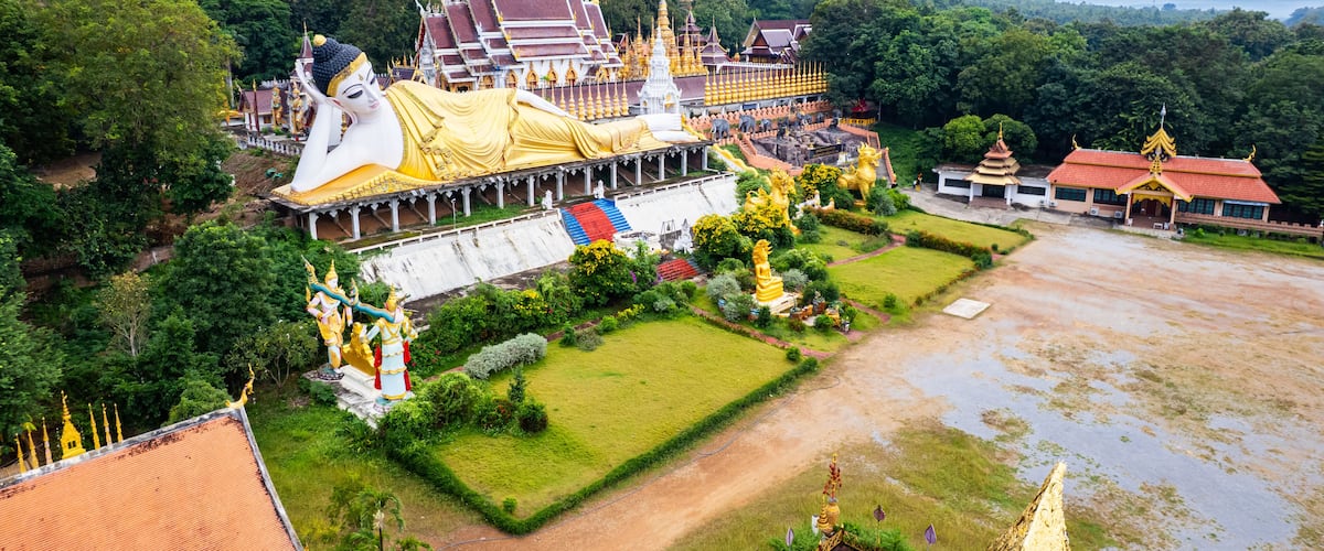 A large temple complex with golden roofs, a large reclining Buddha statue, and lush greenery.
