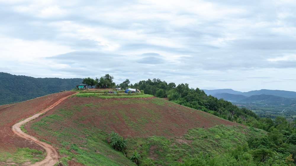 A hilly landscape with a dirt path, green vegetation, and scattered buildings.