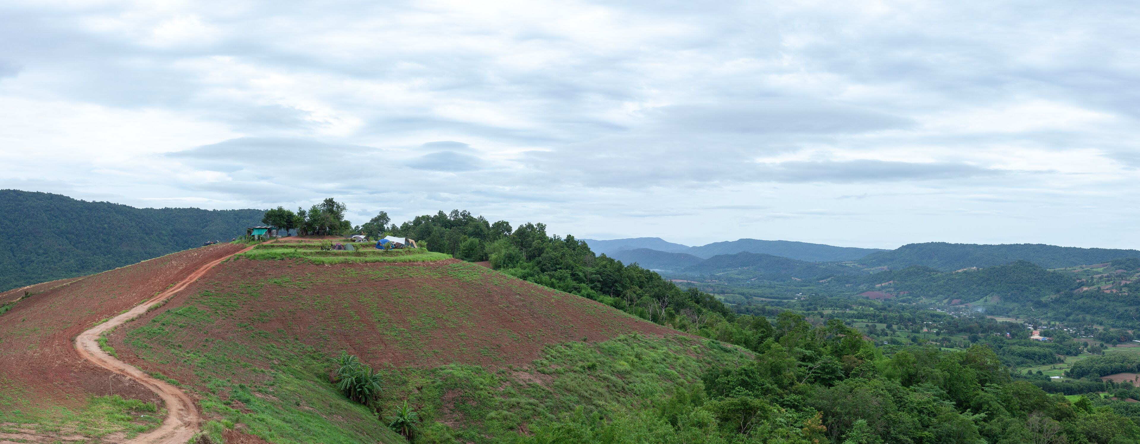 A hilly landscape with a dirt path, green vegetation, and scattered buildings.