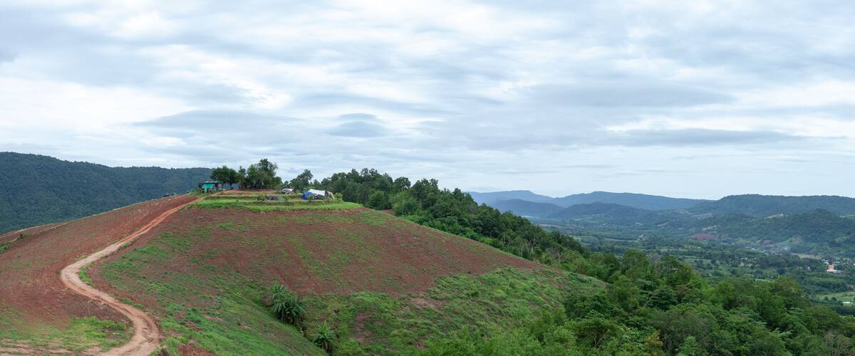 A hilly landscape with a dirt path, green vegetation, and scattered buildings.