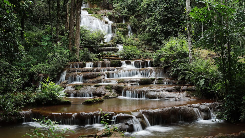A multi-tiered waterfall surrounded by dense forest.