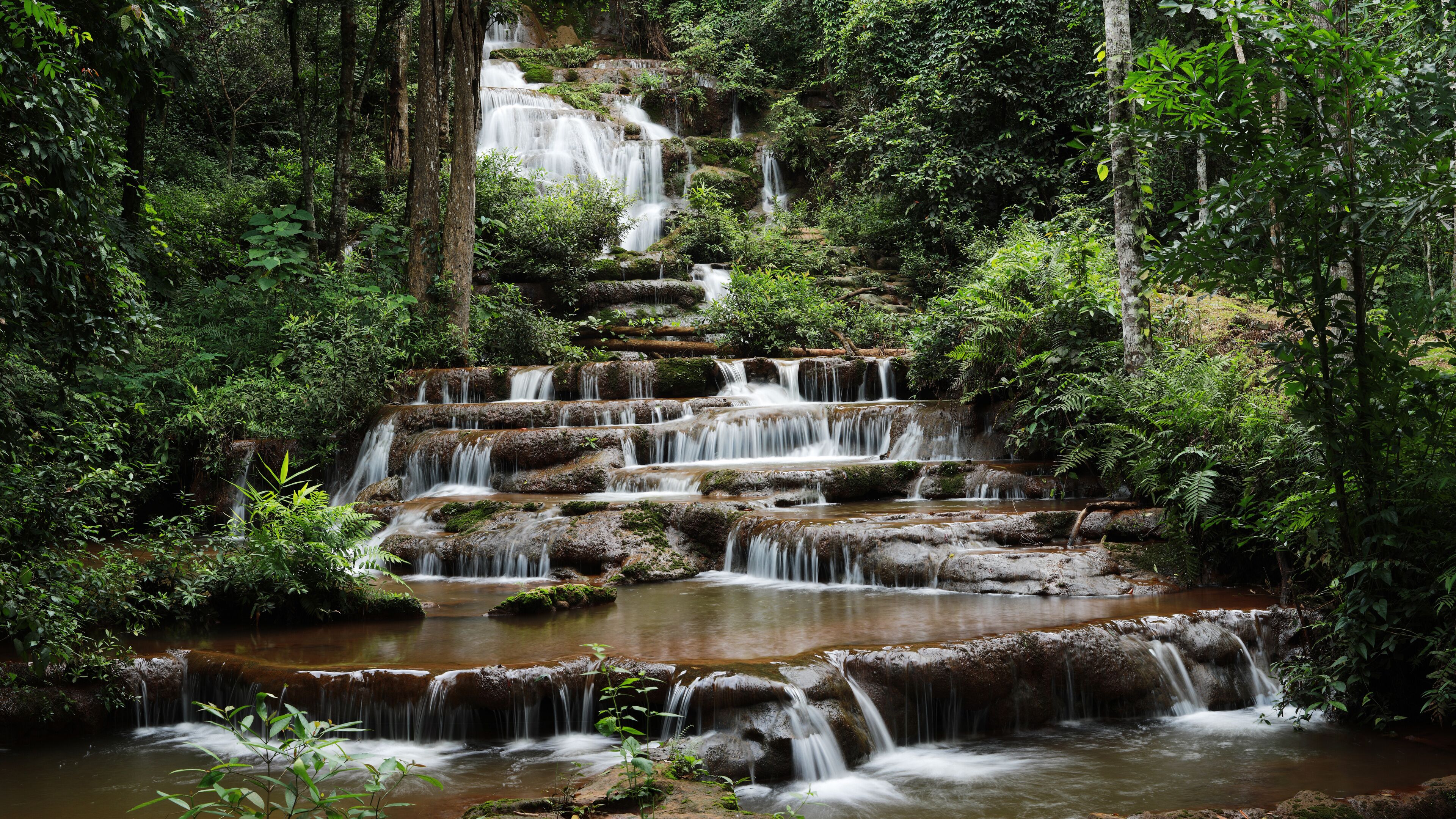 A multi-tiered waterfall surrounded by dense forest.