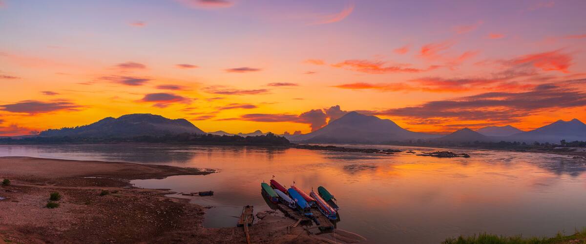A river with boats, mountains, and a sunset.