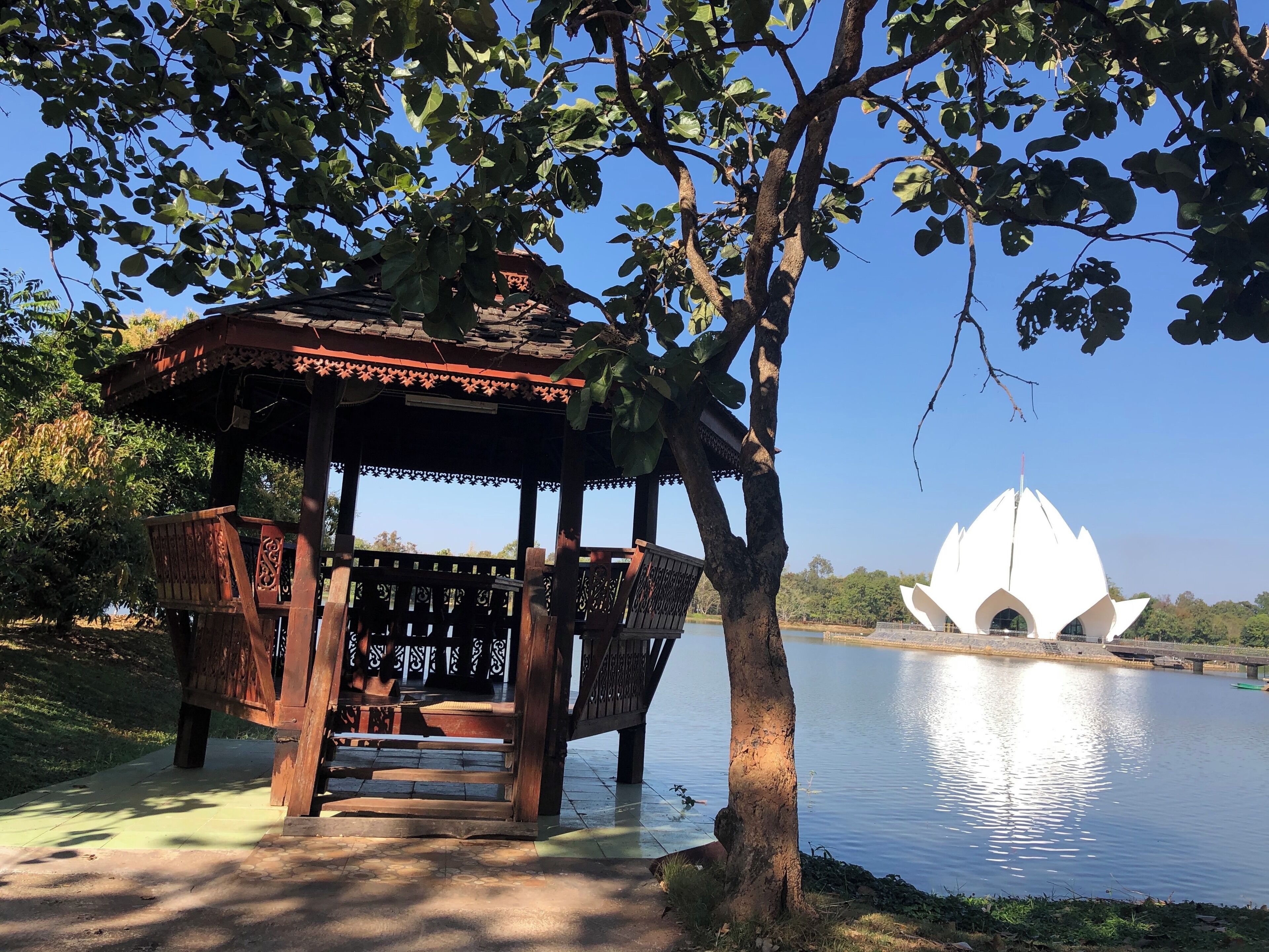 A gazebo by a lake with a lotus-shaped building in the background.
