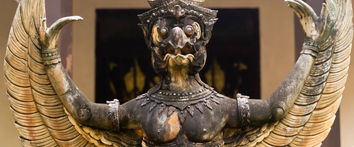 A statue with wings and a pointed hat, set against a plain background.