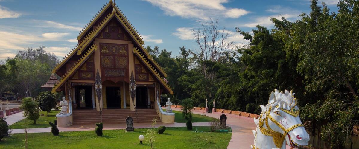 A white horse statue with gold detailing, a traditional building with a golden roof, and a well-maintained garden with a brick pathway.