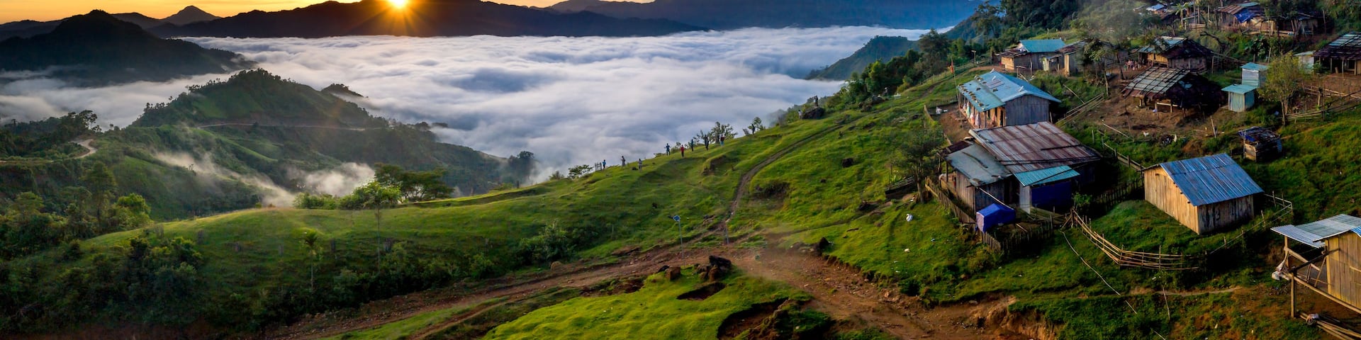 A sunrise over a lush green valley with a village on the hillside.