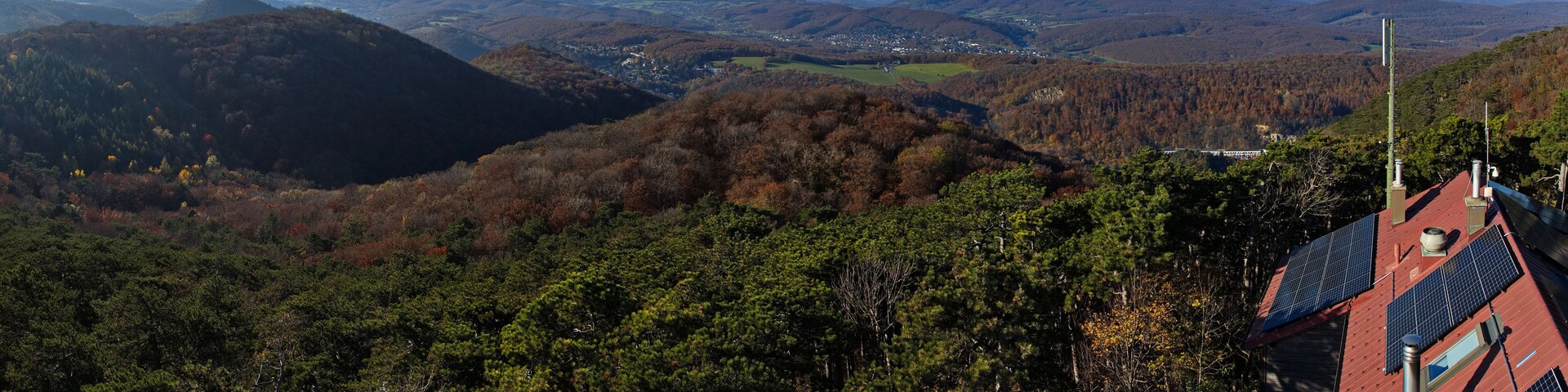 Un paisaje montañoso con bosques densos, un pequeño pueblo en el valle y paneles solares en un edificio.