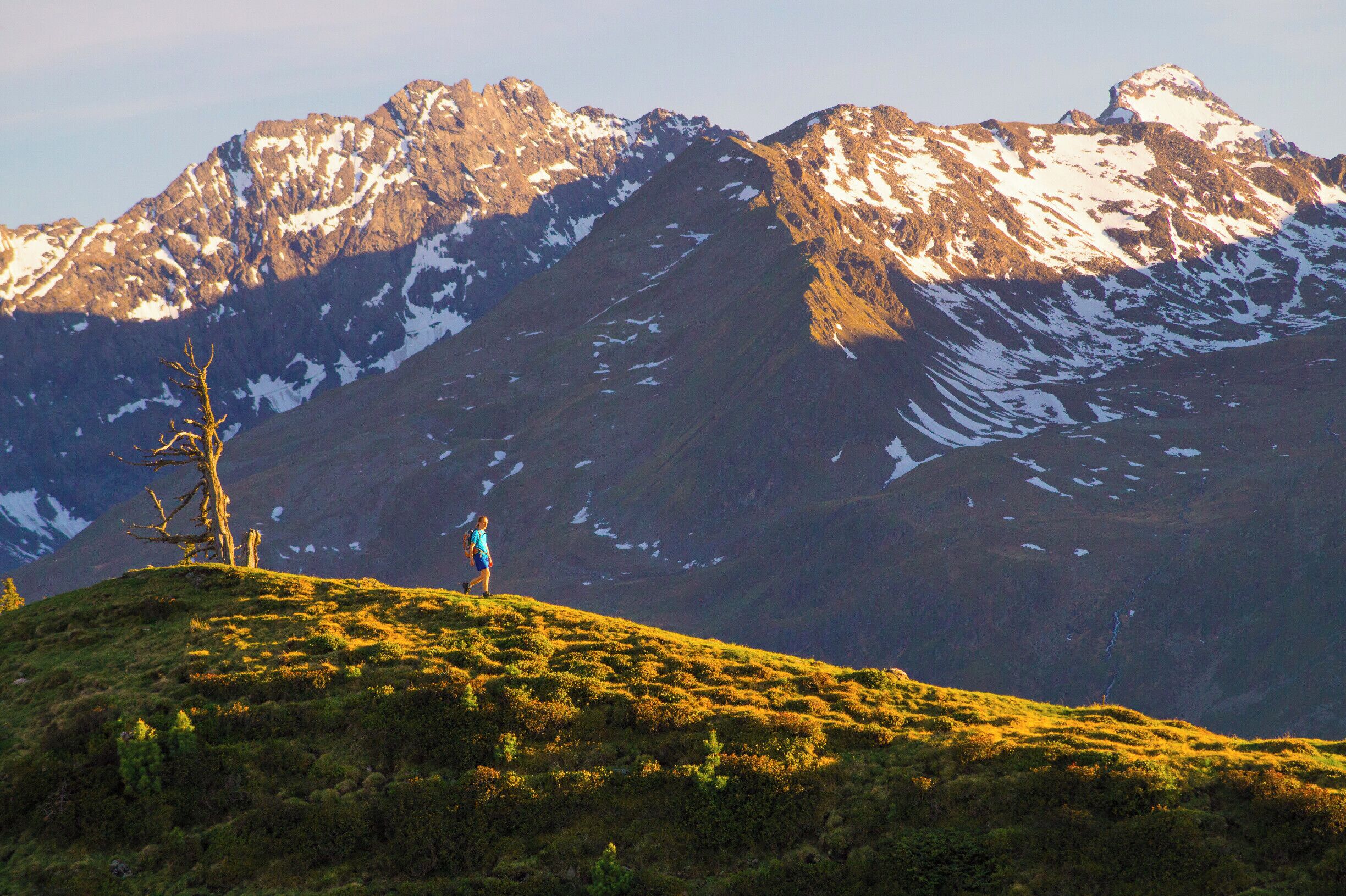 A person walking on a grassy hill with a mountain range in the background.