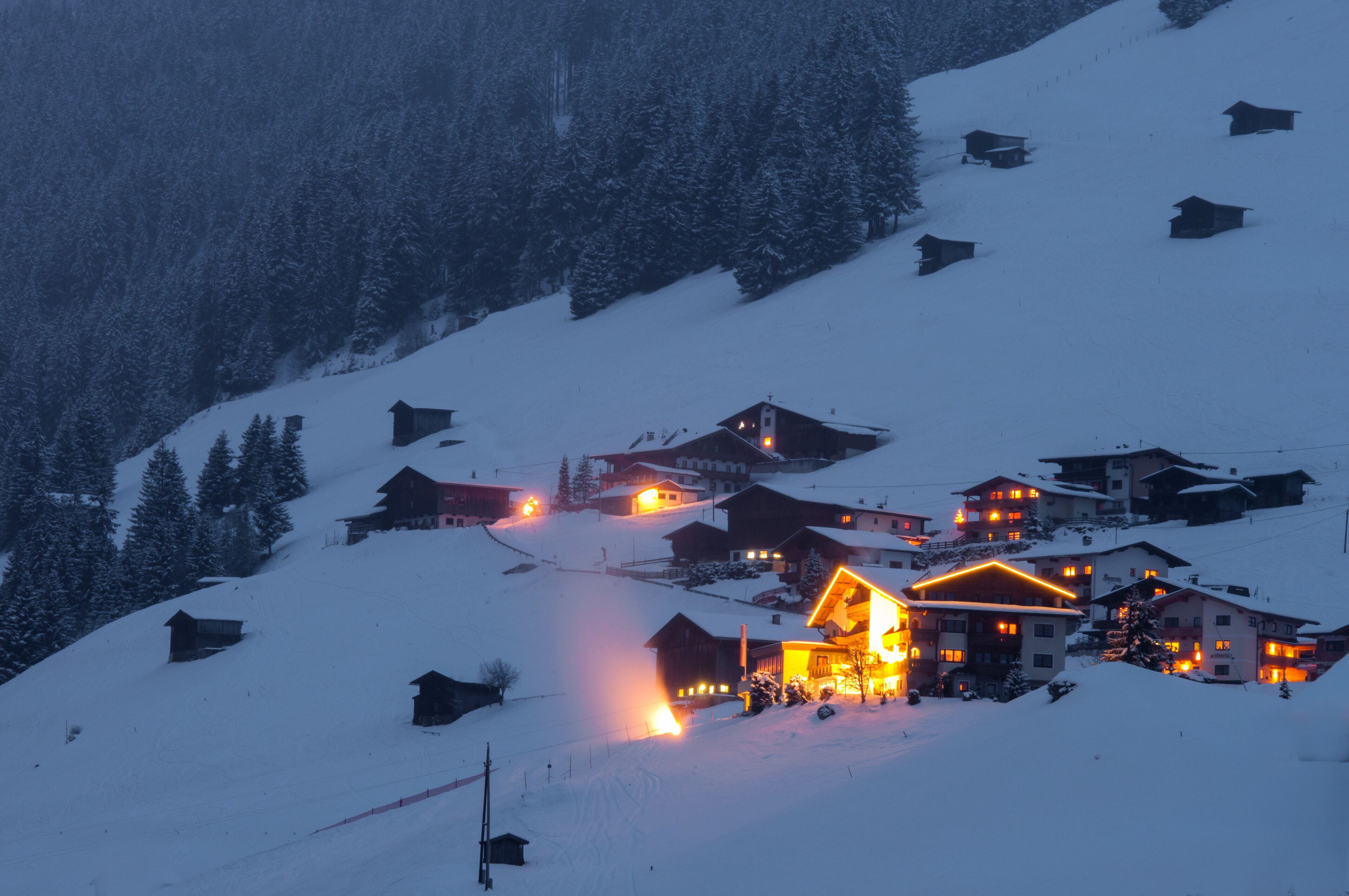 A snow-covered village with illuminated houses at dusk.
