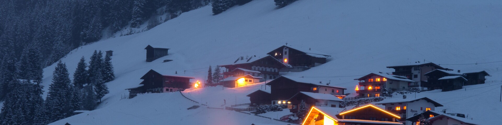 A snow-covered village with illuminated houses at dusk.