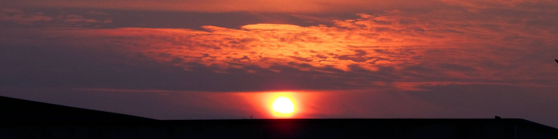 A sunset with the sun partially obscured by clouds, casting a warm glow over the sky.