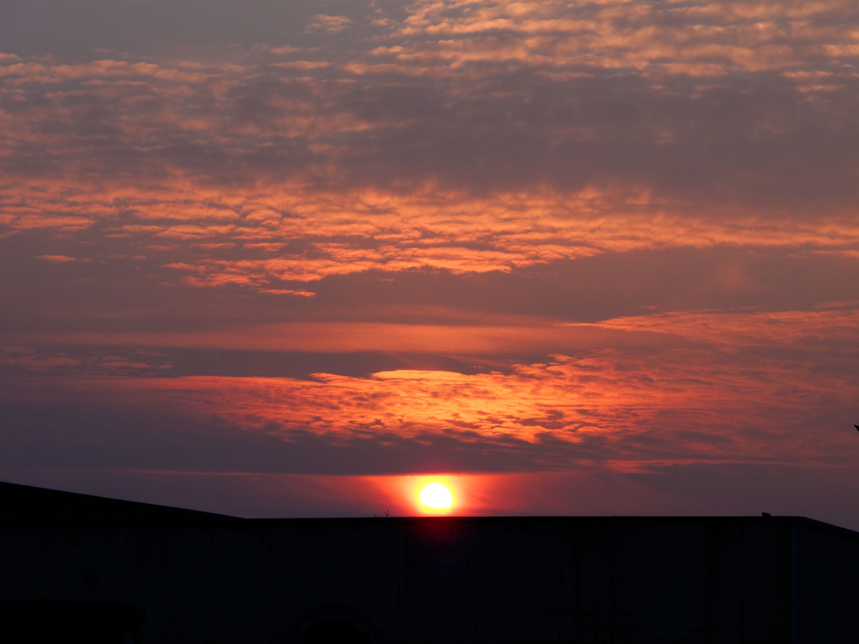 A sunset with the sun partially obscured by clouds, casting a warm glow over the sky.