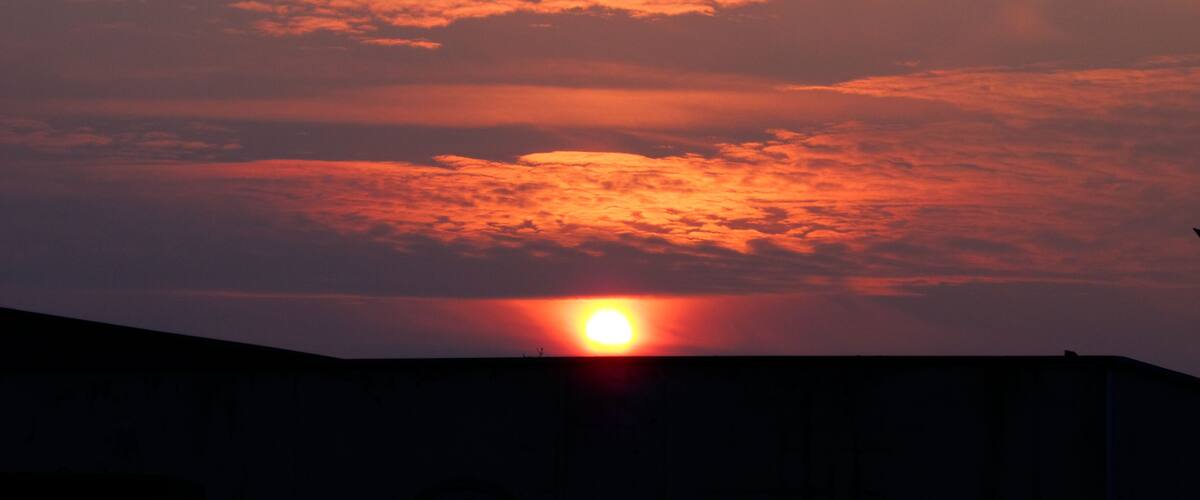 A sunset with the sun partially obscured by clouds, casting a warm glow over the sky.