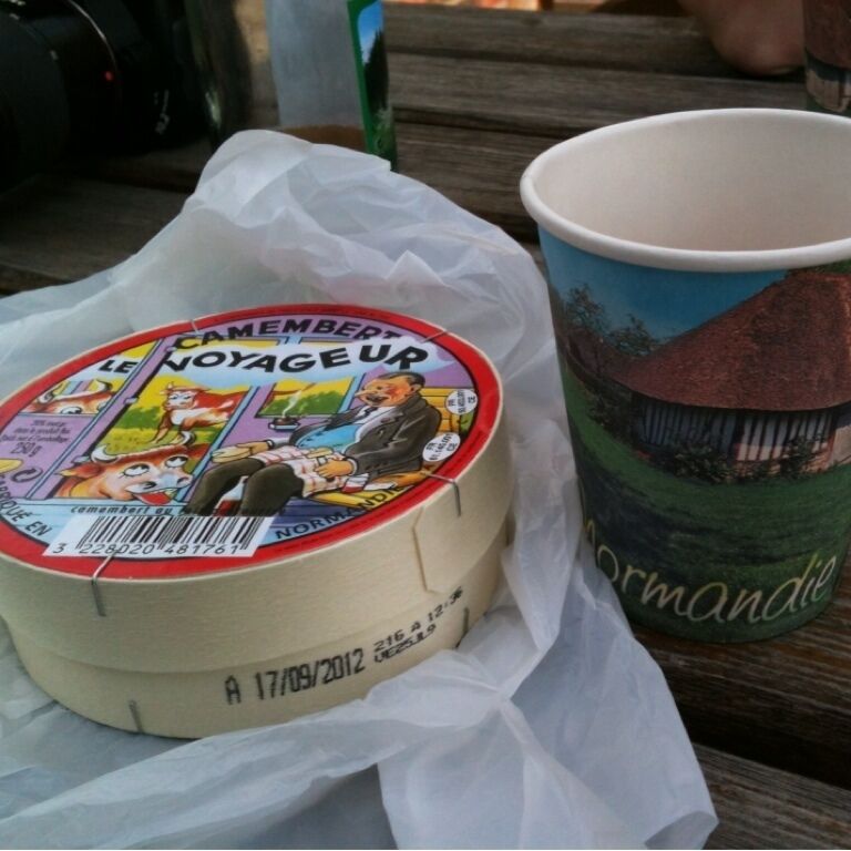 A cheese wheel and a paper cup with a landscape design.