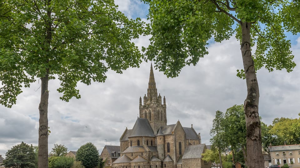A historic church with a tall spire, surrounded by trees and a stone bridge.