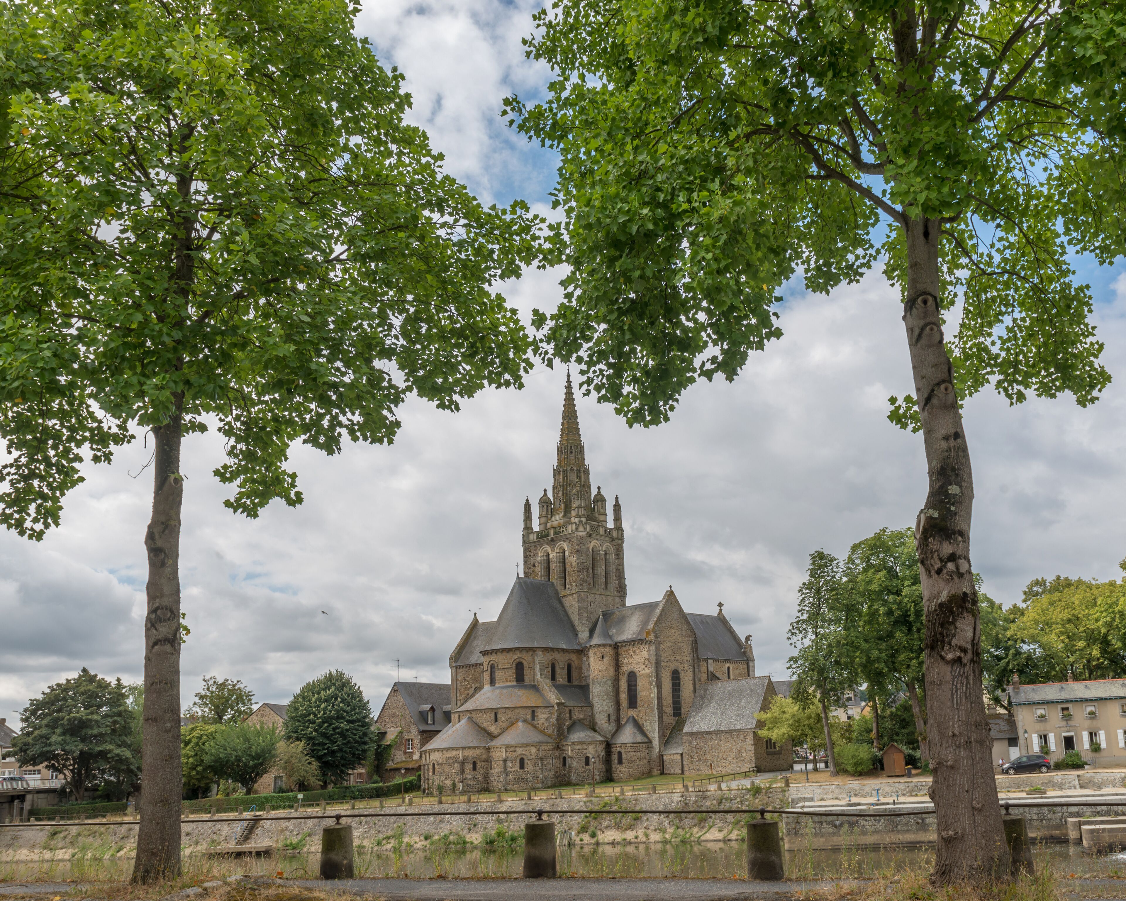A historic church with a tall spire, surrounded by trees and a stone bridge.