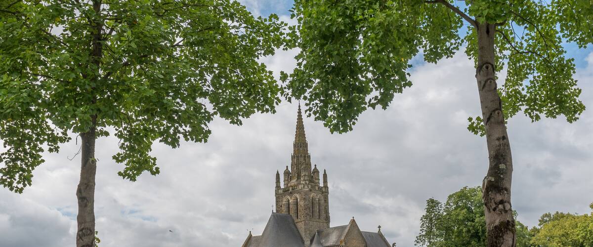 A historic church with a tall spire, surrounded by trees and a stone bridge.