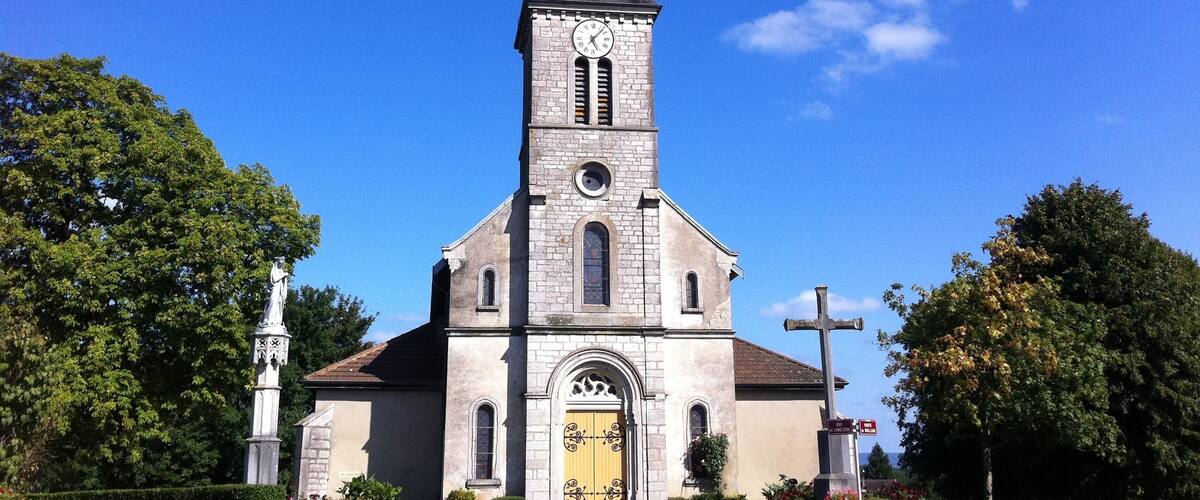 A church with a tall steeple and a clock, surrounded by trees and a cross.