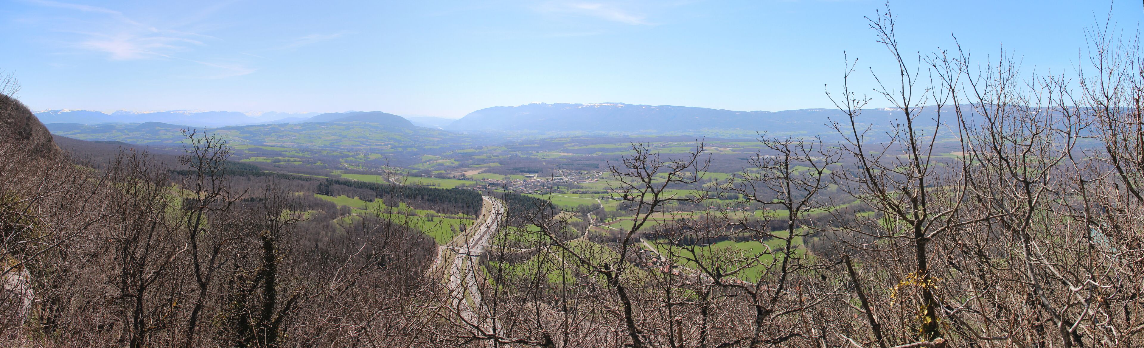A valley with a winding road, surrounded by mountains and sparse trees.