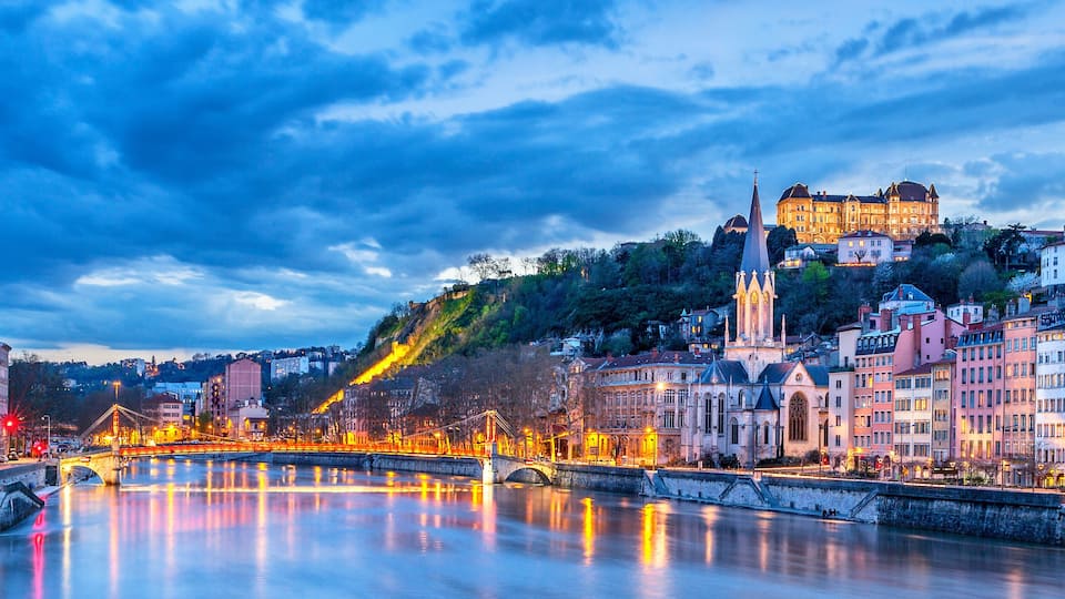 A river with a bridge, historic buildings, and a castle on a hill.