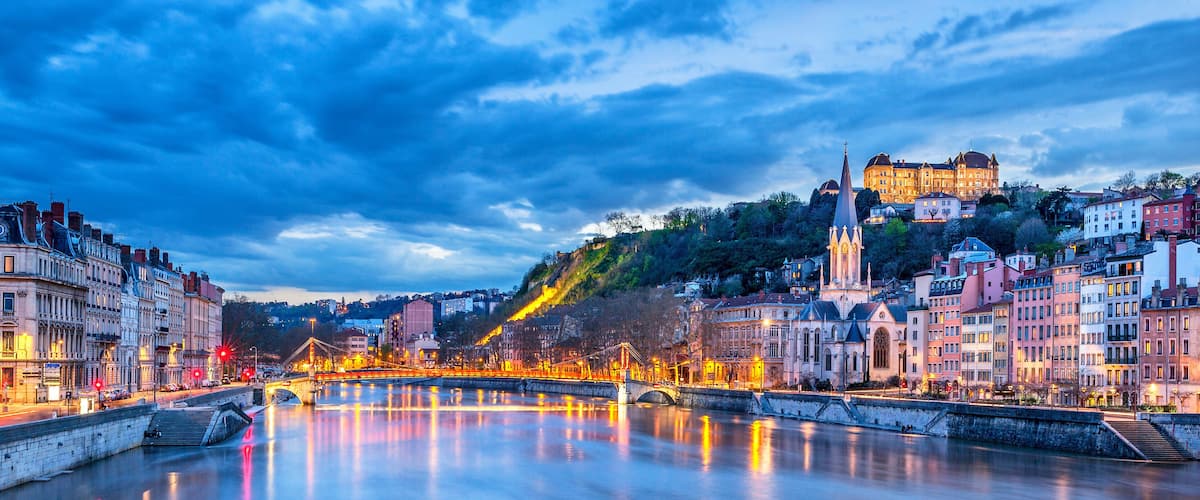 A river with a bridge, historic buildings, and a castle on a hill.