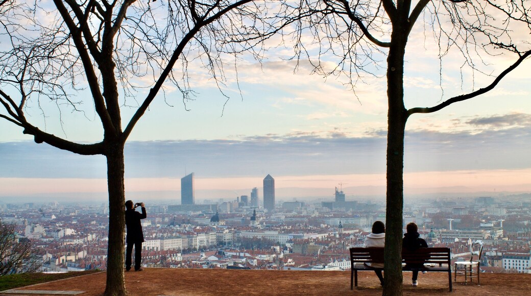 2 people sitting on a bench admiring a wonderful sunrise over the city of Lyon in France with a tourist taking picture of the view
