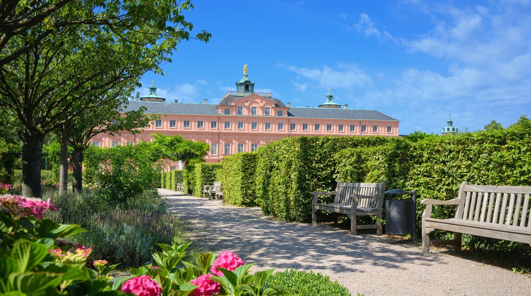 A large pink building with a green roof, surrounded by lush greenery and a gravel path.