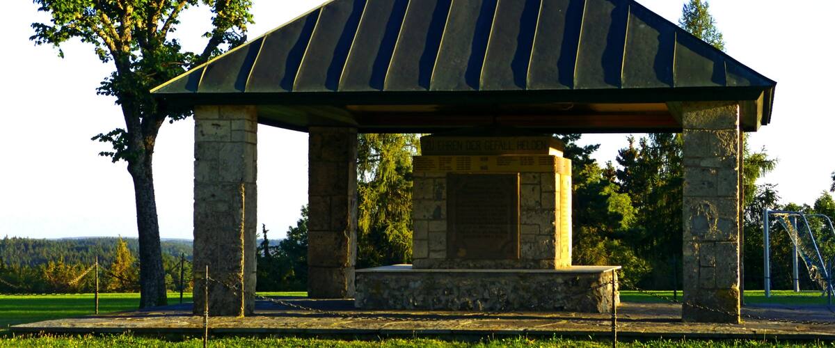 A gazebo with a weather vane, surrounded by grass and trees.