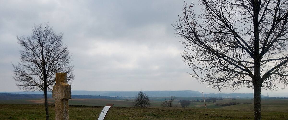 A park with a bench, informational signs, and a view of distant hills.