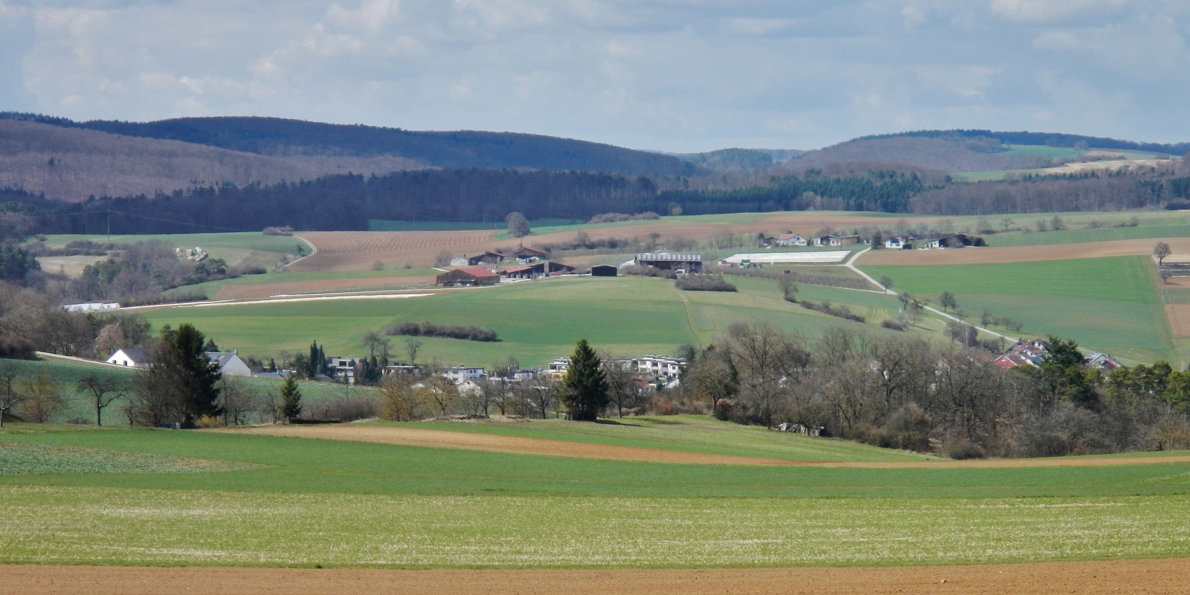 A rural landscape with rolling hills, fields, and scattered houses.