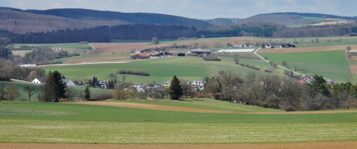 A rural landscape with rolling hills, fields, and scattered houses.