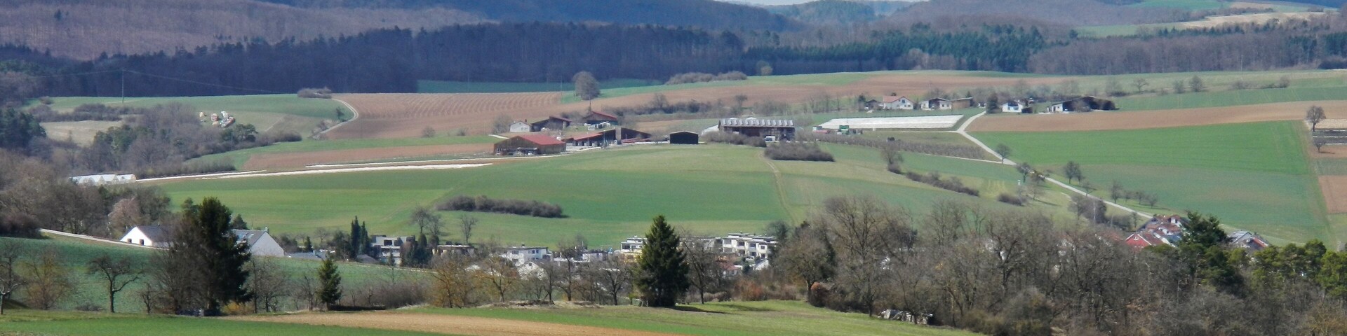 A rural landscape with rolling hills, fields, and scattered houses.