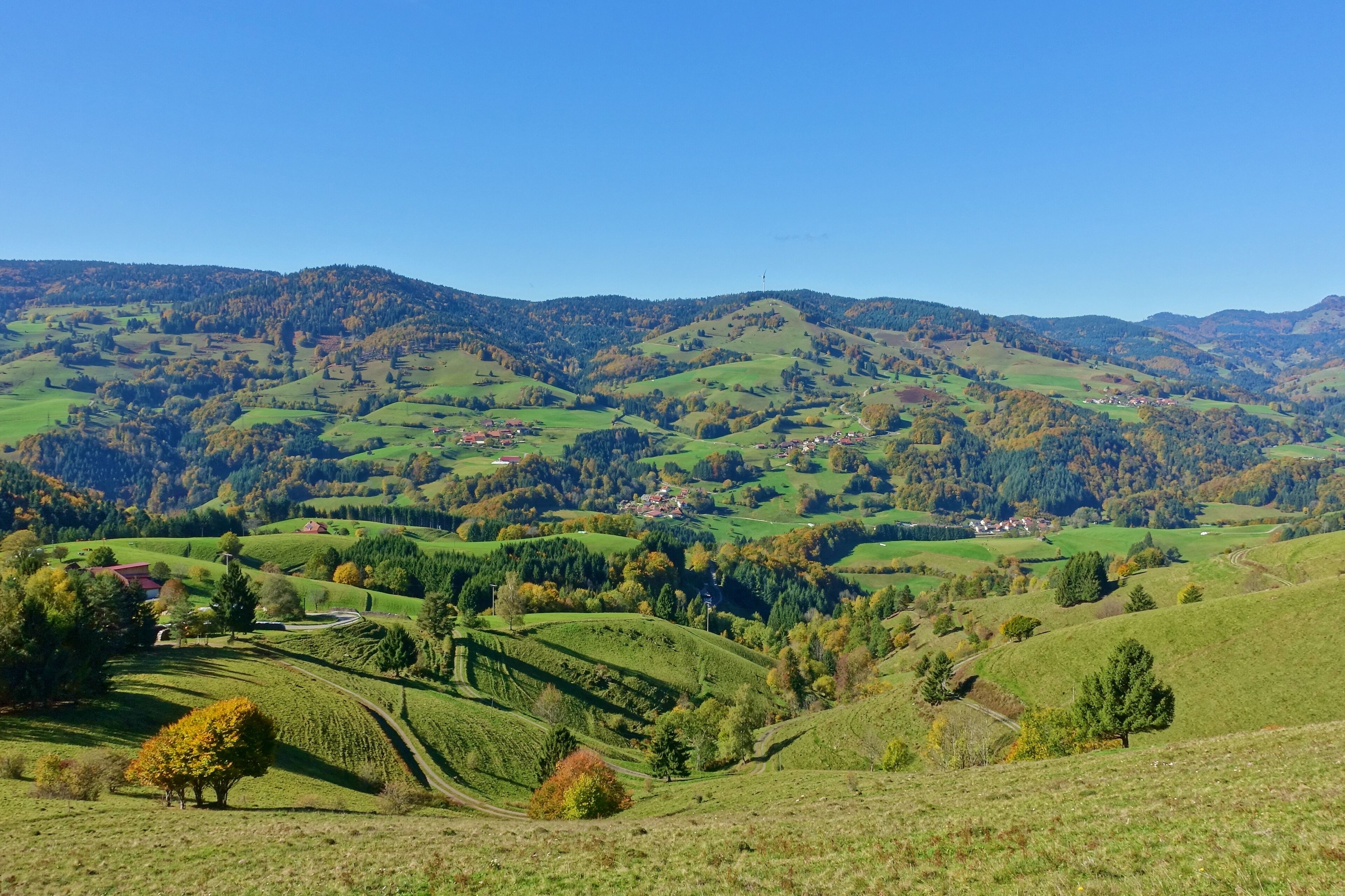 Rolling green hills, a small village, and distant mountains under a clear blue sky.