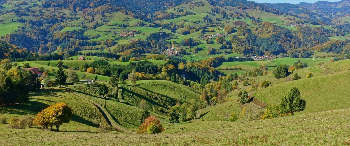 Rolling green hills, a small village, and distant mountains under a clear blue sky.