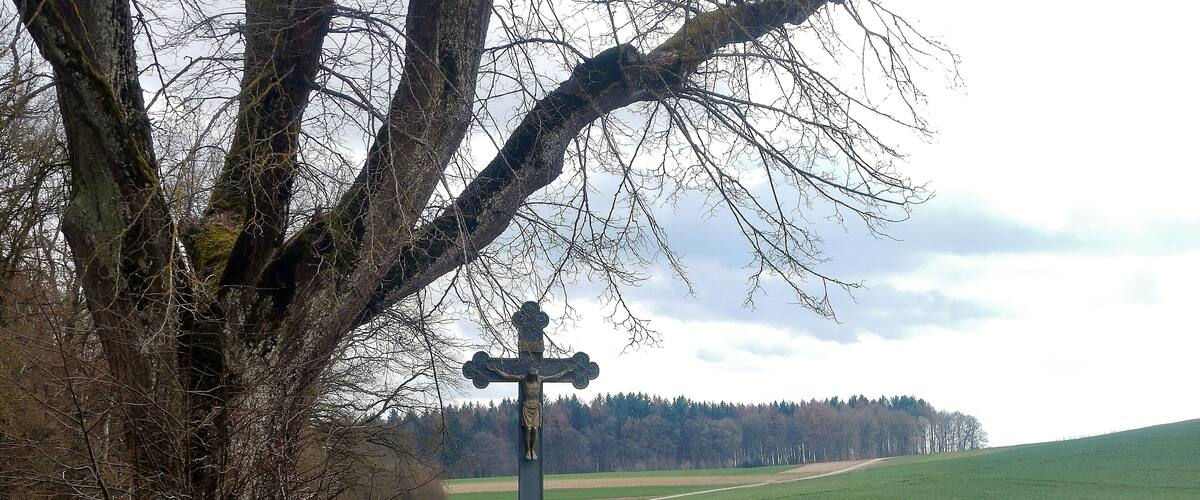 A rural landscape with a cross monument and a winding road.