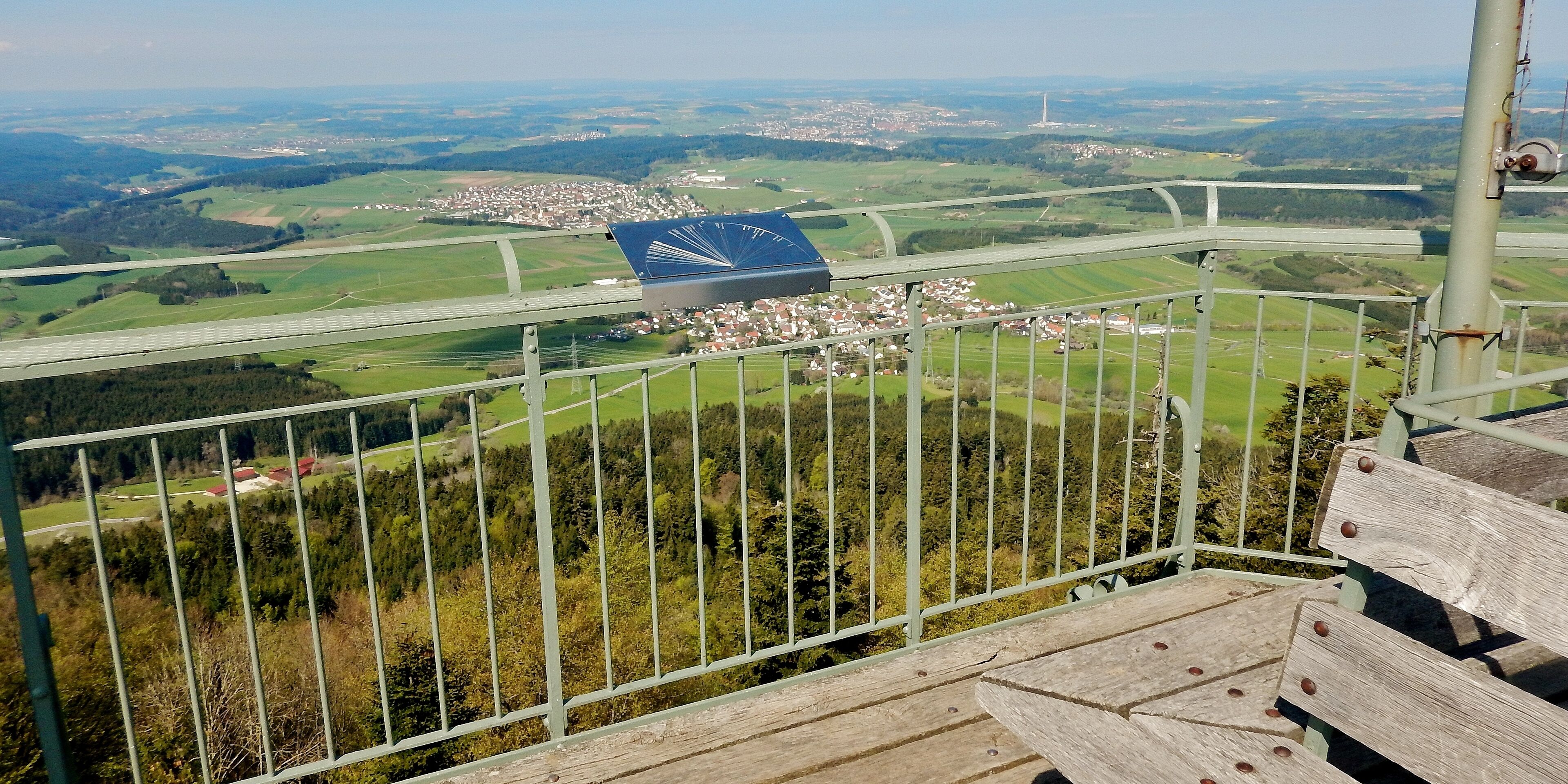 A scenic overlook with a view of a town, green fields, and a distant tower.