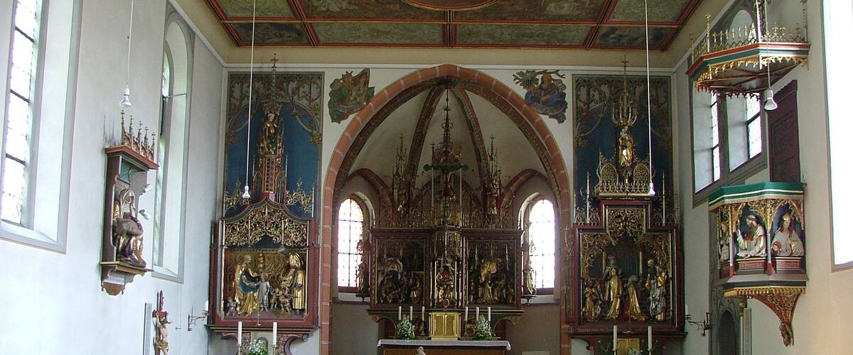 An ornate church interior with wooden pews, a central altar, and detailed frescoes on the ceiling.