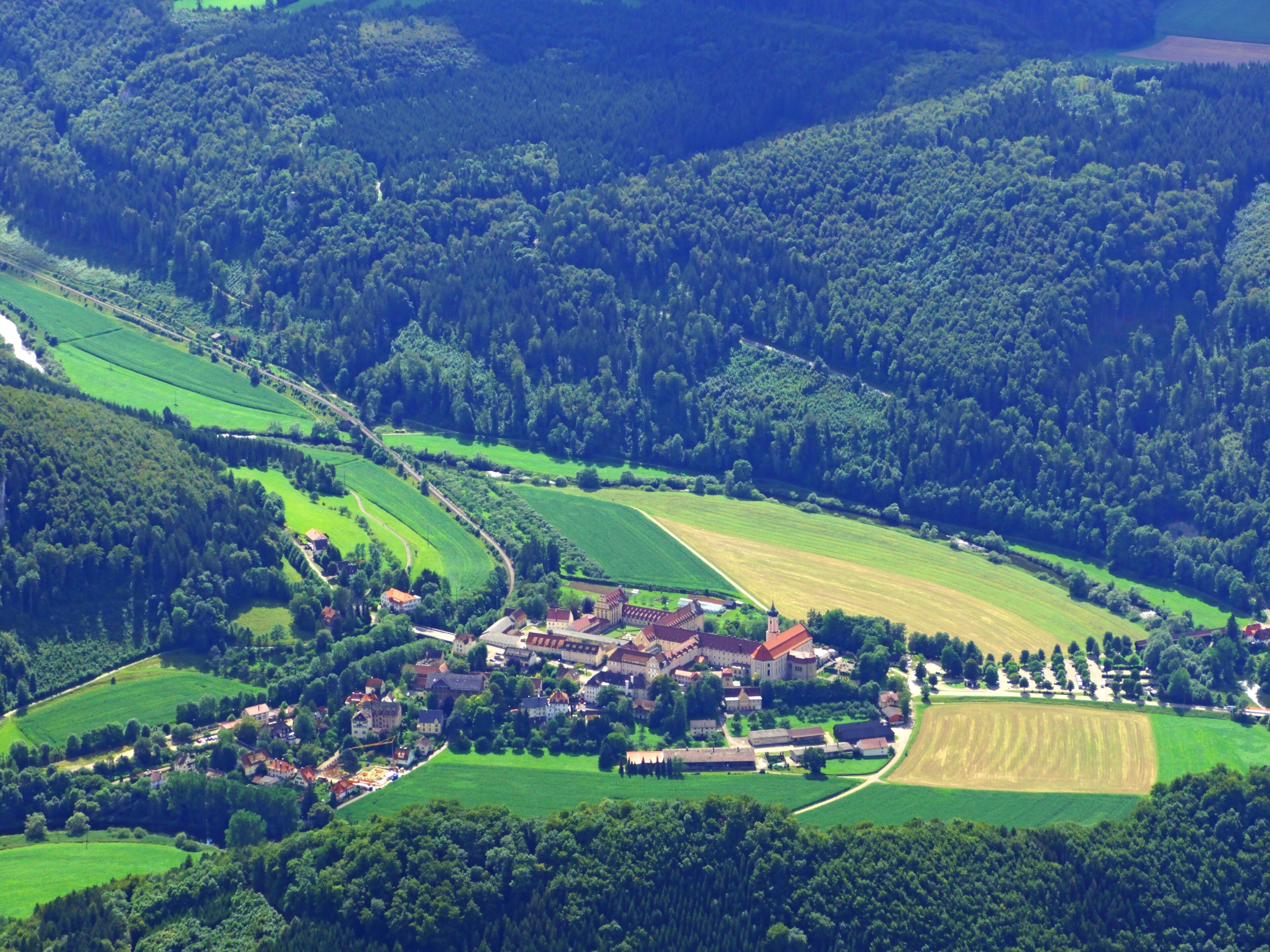 An aerial view of a rural village surrounded by lush green fields and dense forests.