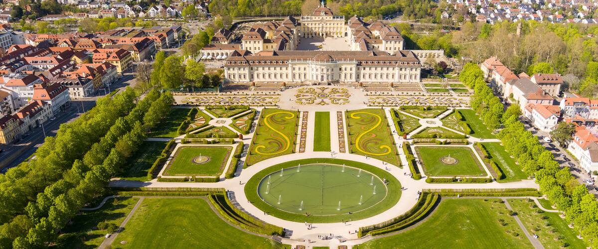 Vista aérea de un palacio imponente con un jardín simétrico, rodeado de edificios residenciales.