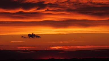 A sunset with orange and red clouds over a mountainous landscape.