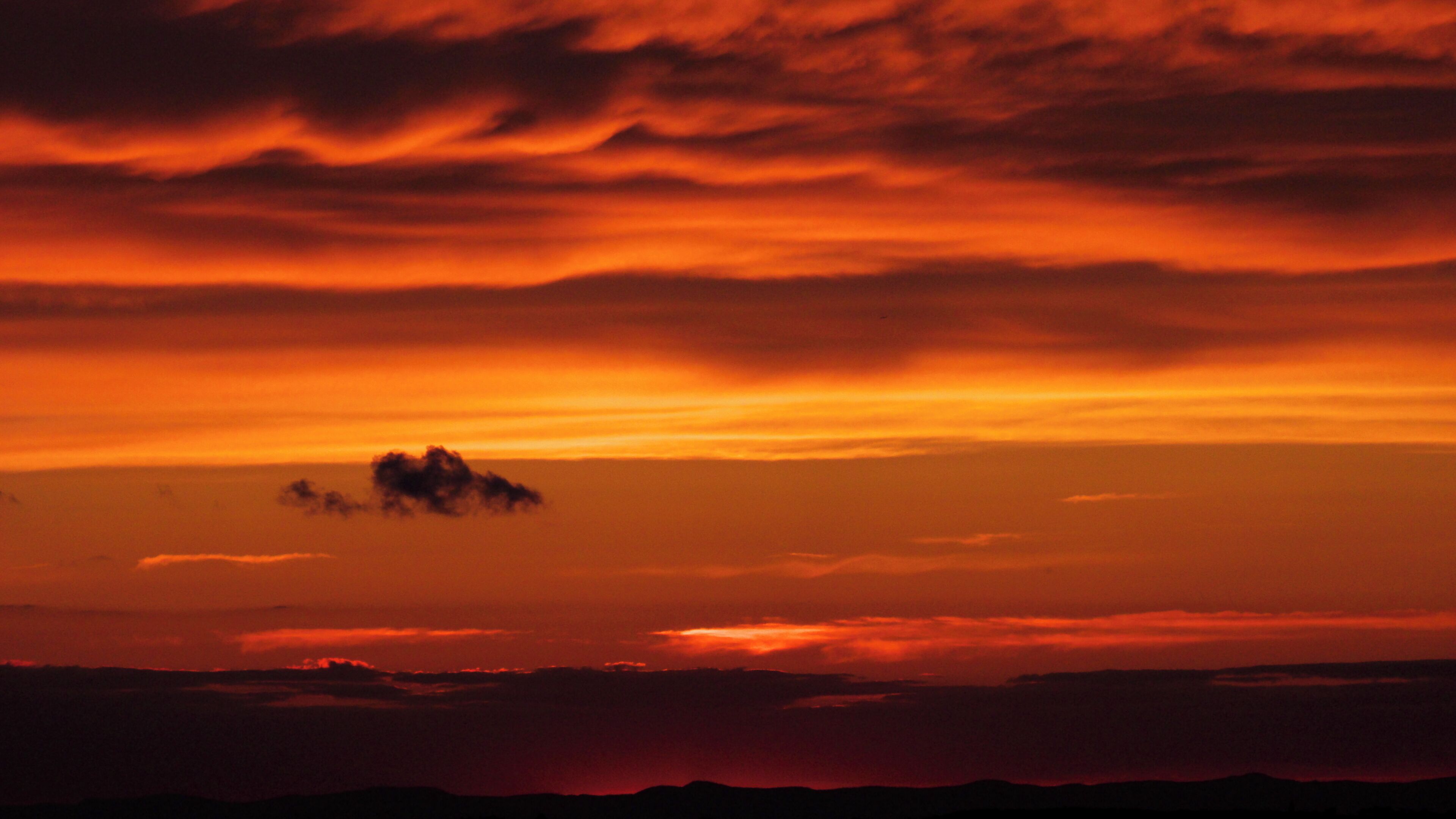A sunset with orange and red clouds over a mountainous landscape.