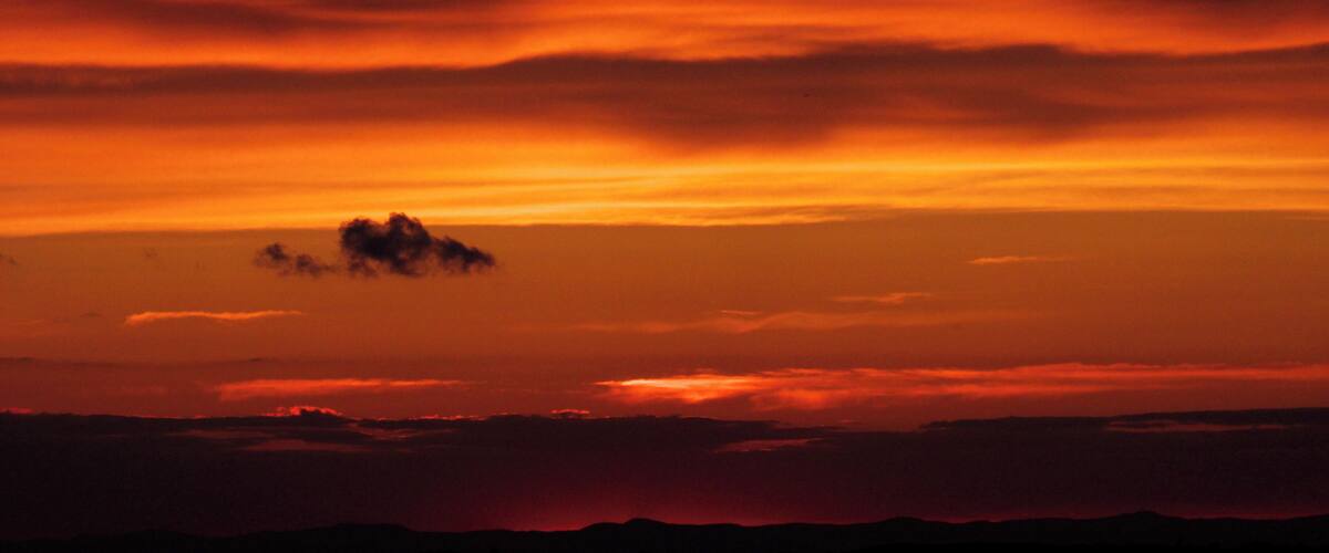 A sunset with orange and red clouds over a mountainous landscape.