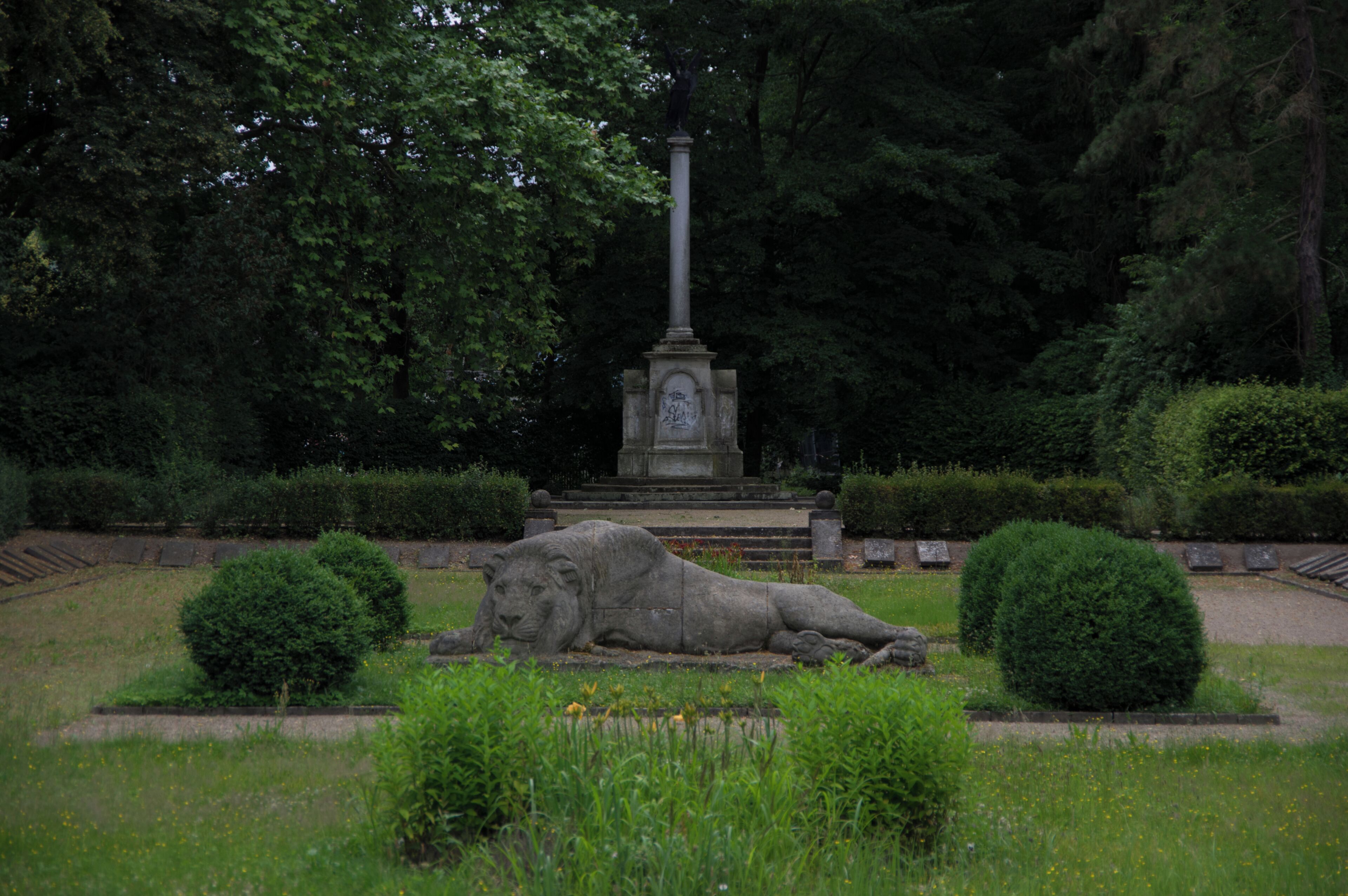 A stone lion statue in a park with a monument in the background.