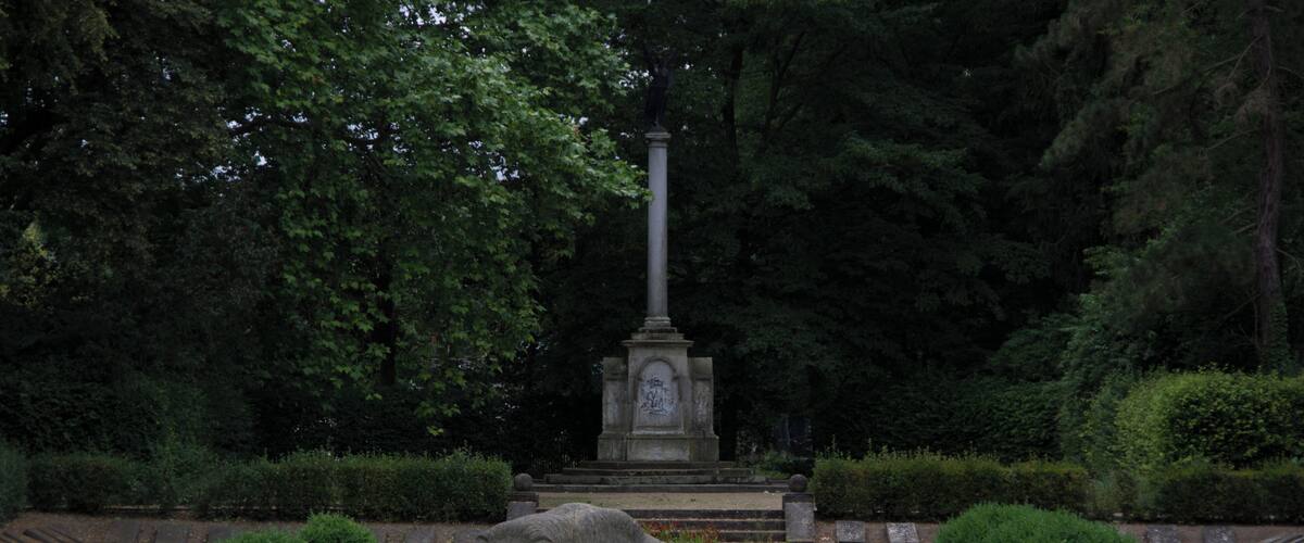 A stone lion statue in a park with a monument in the background.