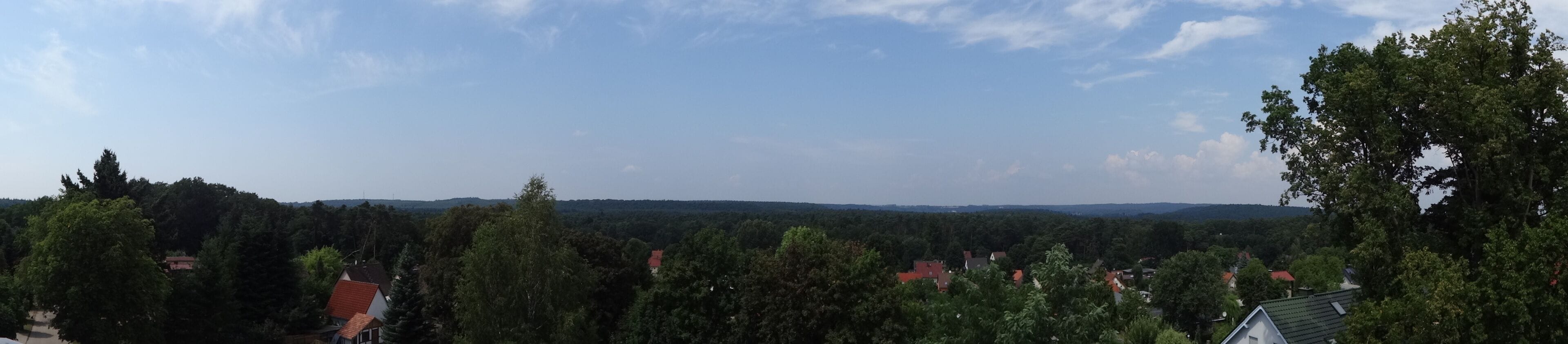 A rural landscape with dense trees, scattered houses, and distant hills under a clear sky.